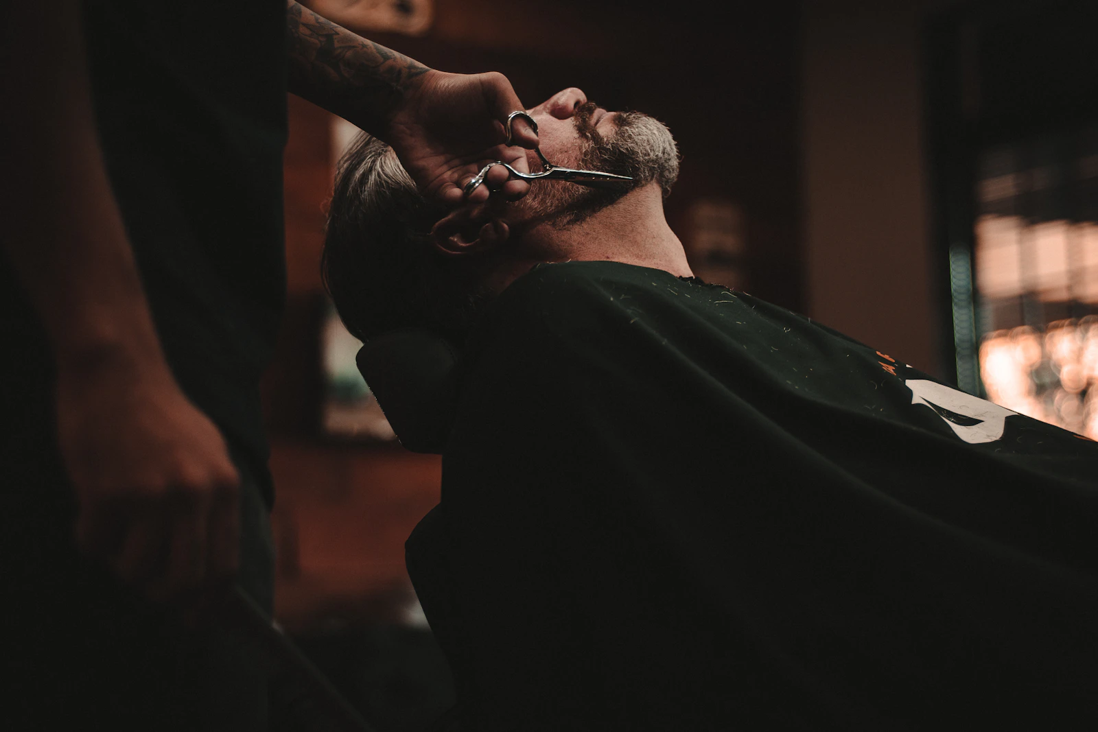 A barber carefully shaping a customer's beard with scissors; illustrative stock photograph