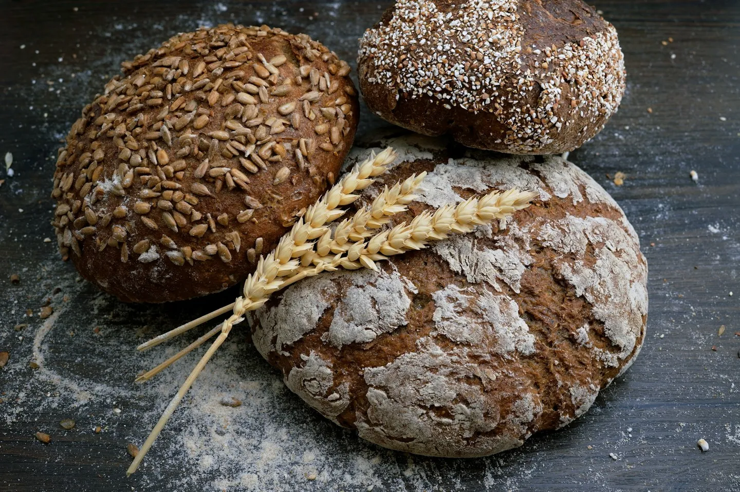 Flour-dusted and seeded loaves on a dark wooden table; illustrative stock photograph
